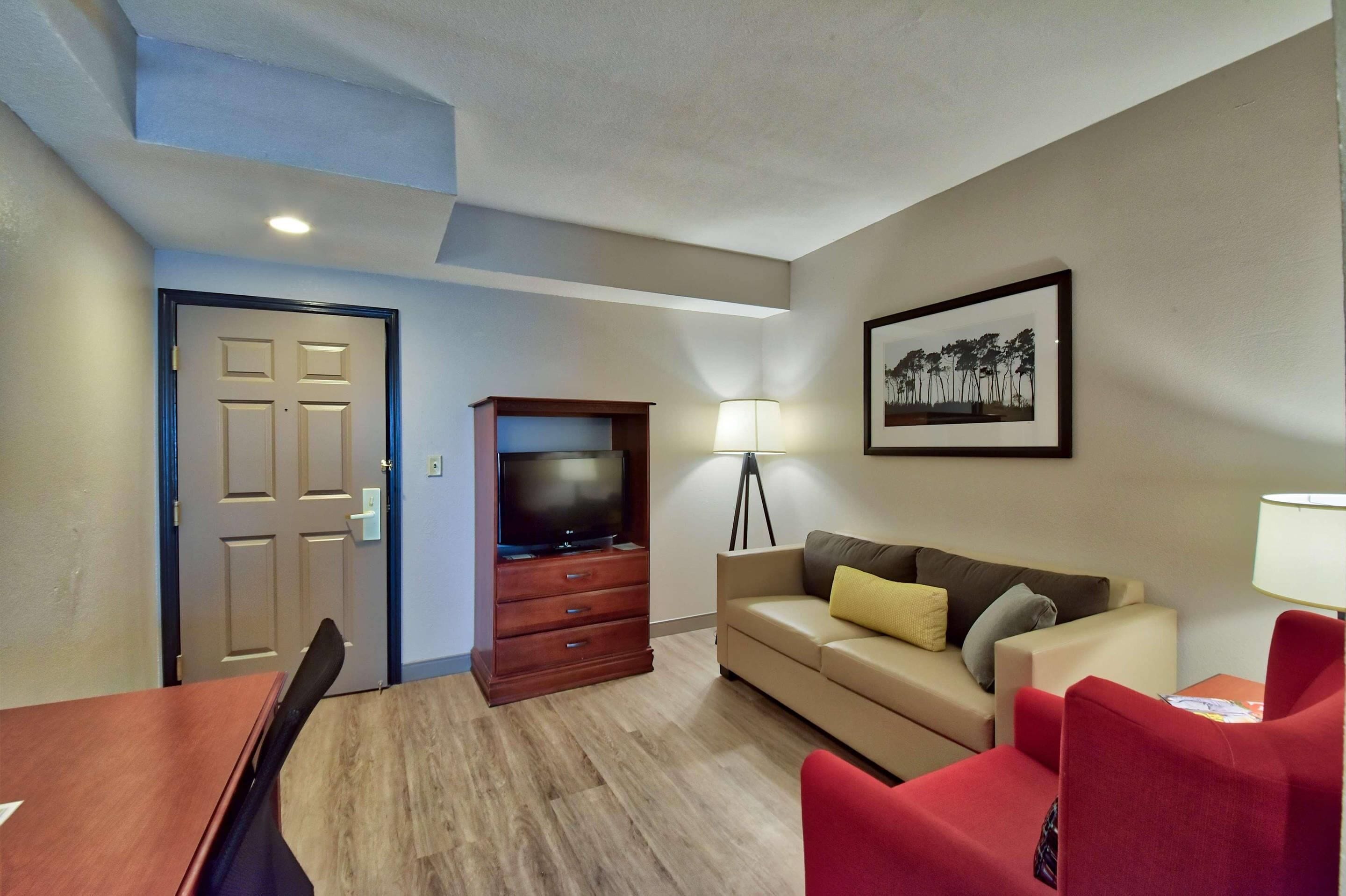 A modern living room with a wooden TV stand, a beige sofa, red chairs, a dining table, and a framed picture on the wall.
