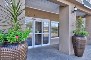 A building entrance with a glass door, large potted plants, and a wall-mounted light fixture. - Country Inn & Suites by Radisson, Ocala Southwest (Ocala)