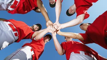 A group of people in red and white sports uniforms forming a circle with their hands together.