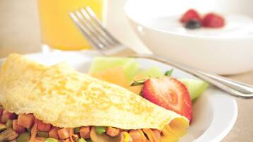 A breakfast plate with an omelette, vegetables, and fruit, a glass of orange juice, and a bowl of yogurt with berries.