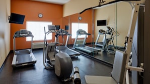 Une salle de sport équipée de tapis de course, de vélos elliptiques et d’une machine de musculation.
