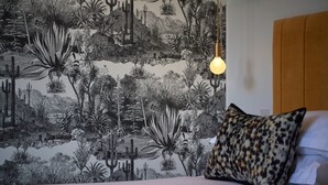 Un dormitorio con un mural de flora del desierto en la pared, una cama con almohada estampada y una lámpara colgante.