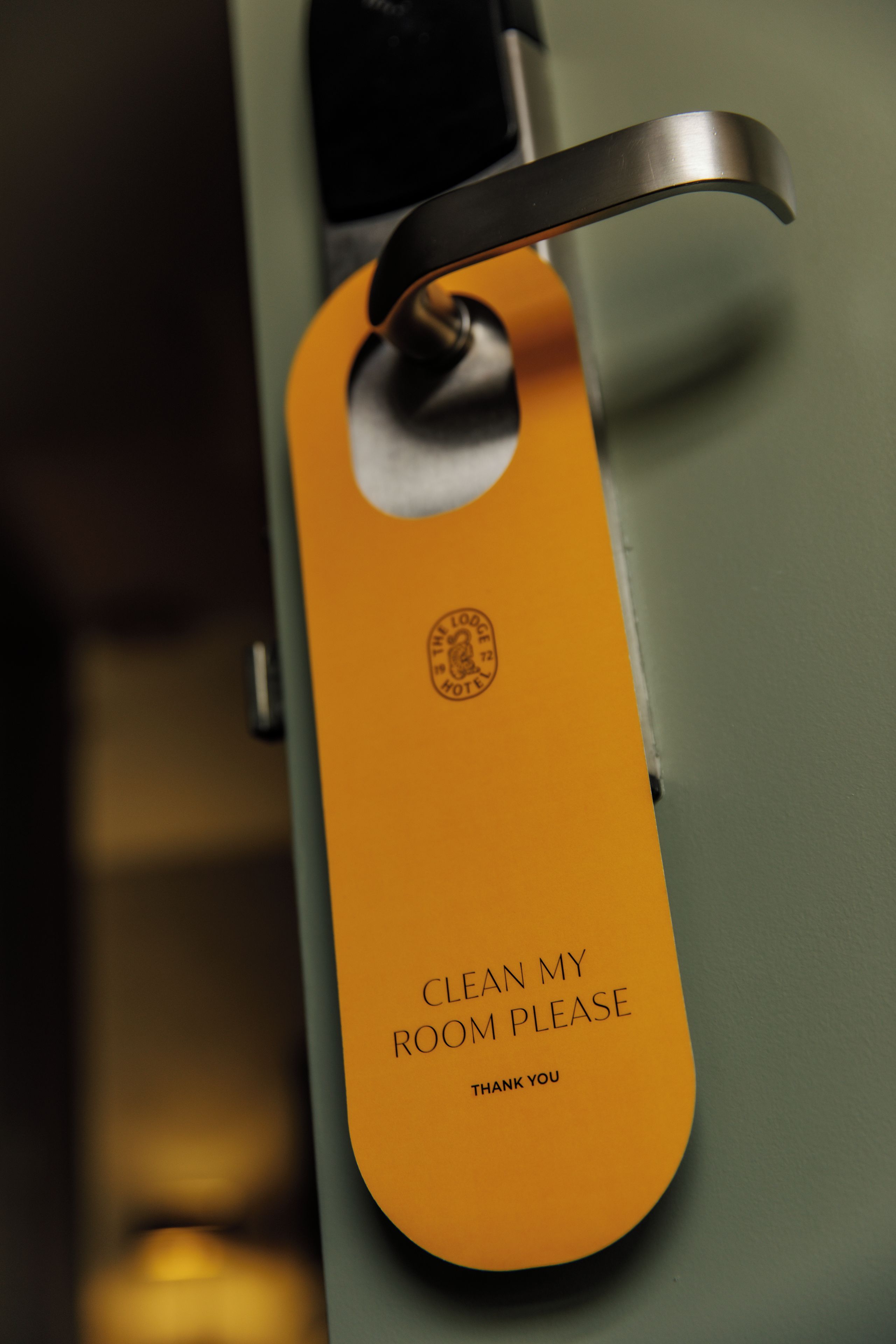 A hotel room door with a 'Clean My Room Please' sign attached to the handle.