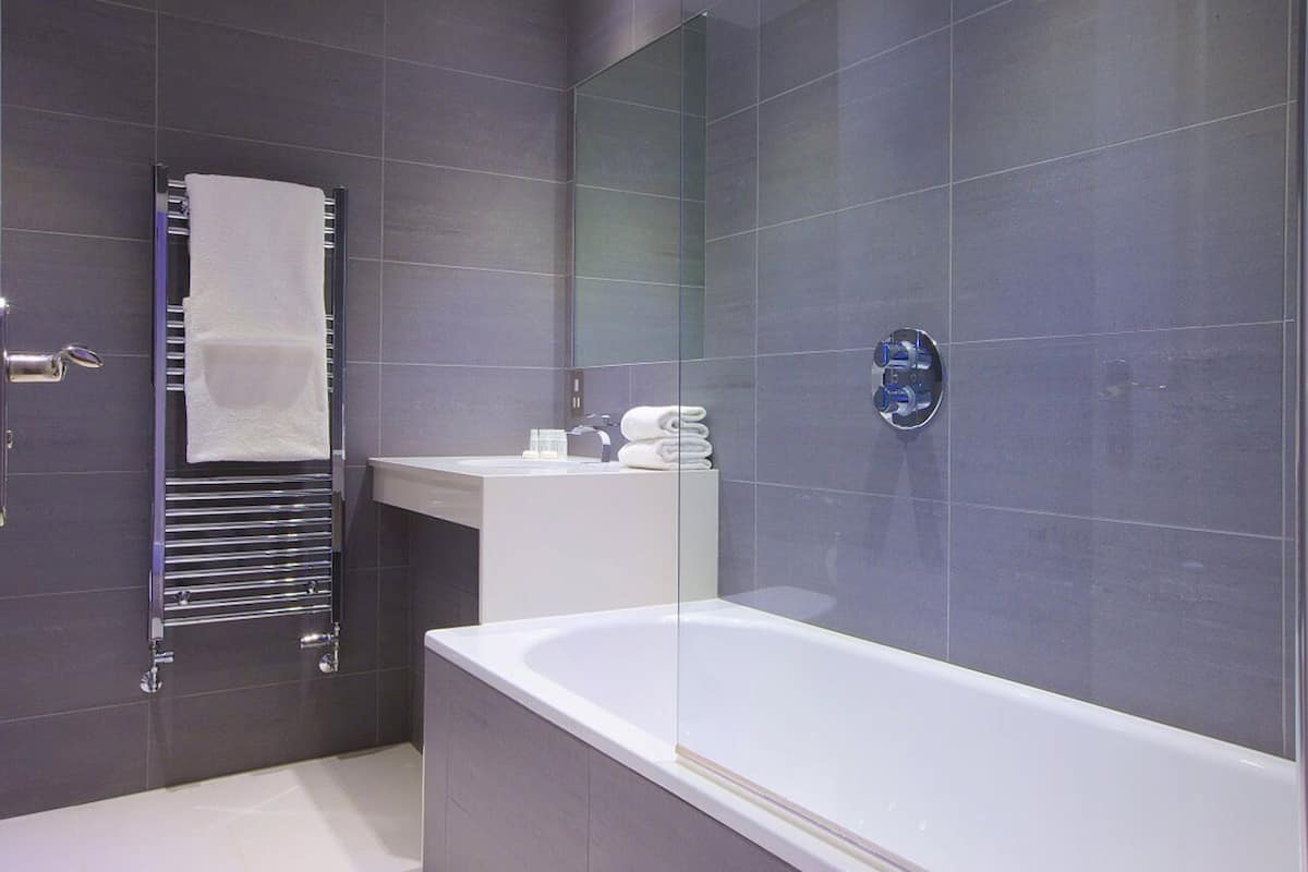A modern bathroom with a glass-enclosed shower, a white bathtub, and a towel rack with folded towels.