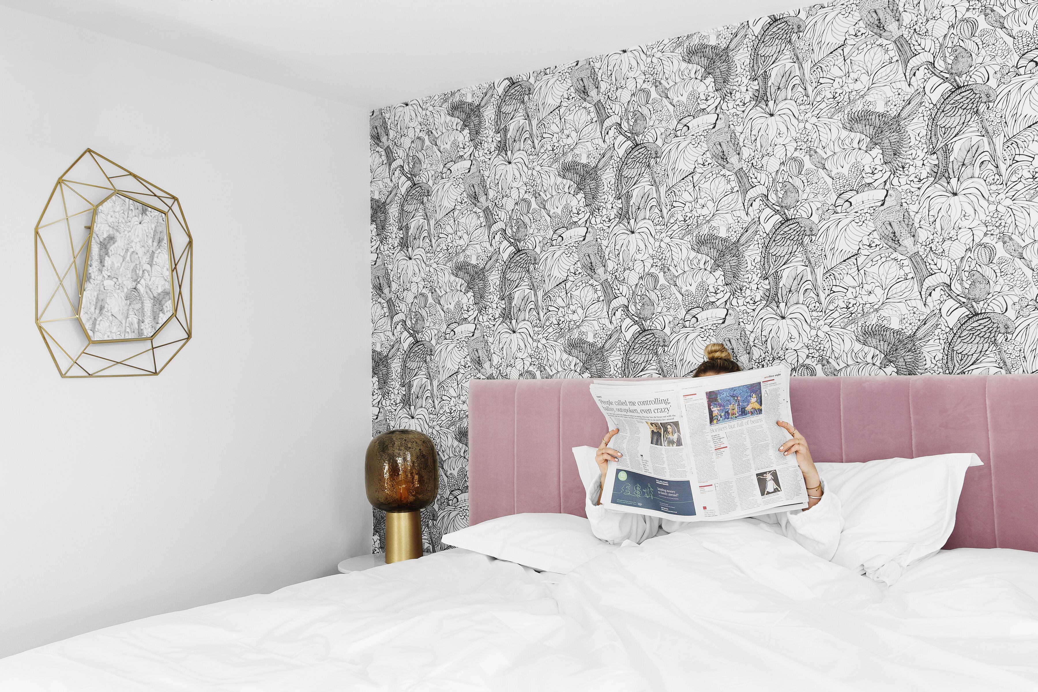 Een slaapkamer met behang met een patroon, een kunstwerk met geometrische vormen en een bedlamp.