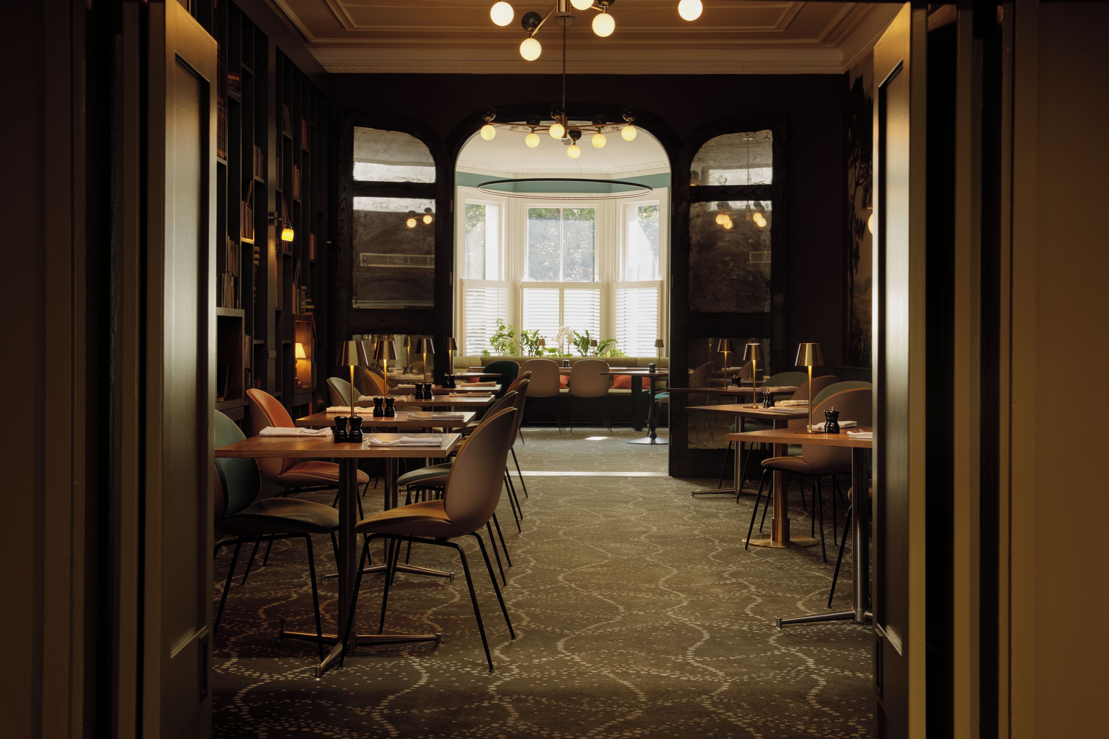 A restaurant with a long table layout, multiple seating options, and a view through a large arched window.