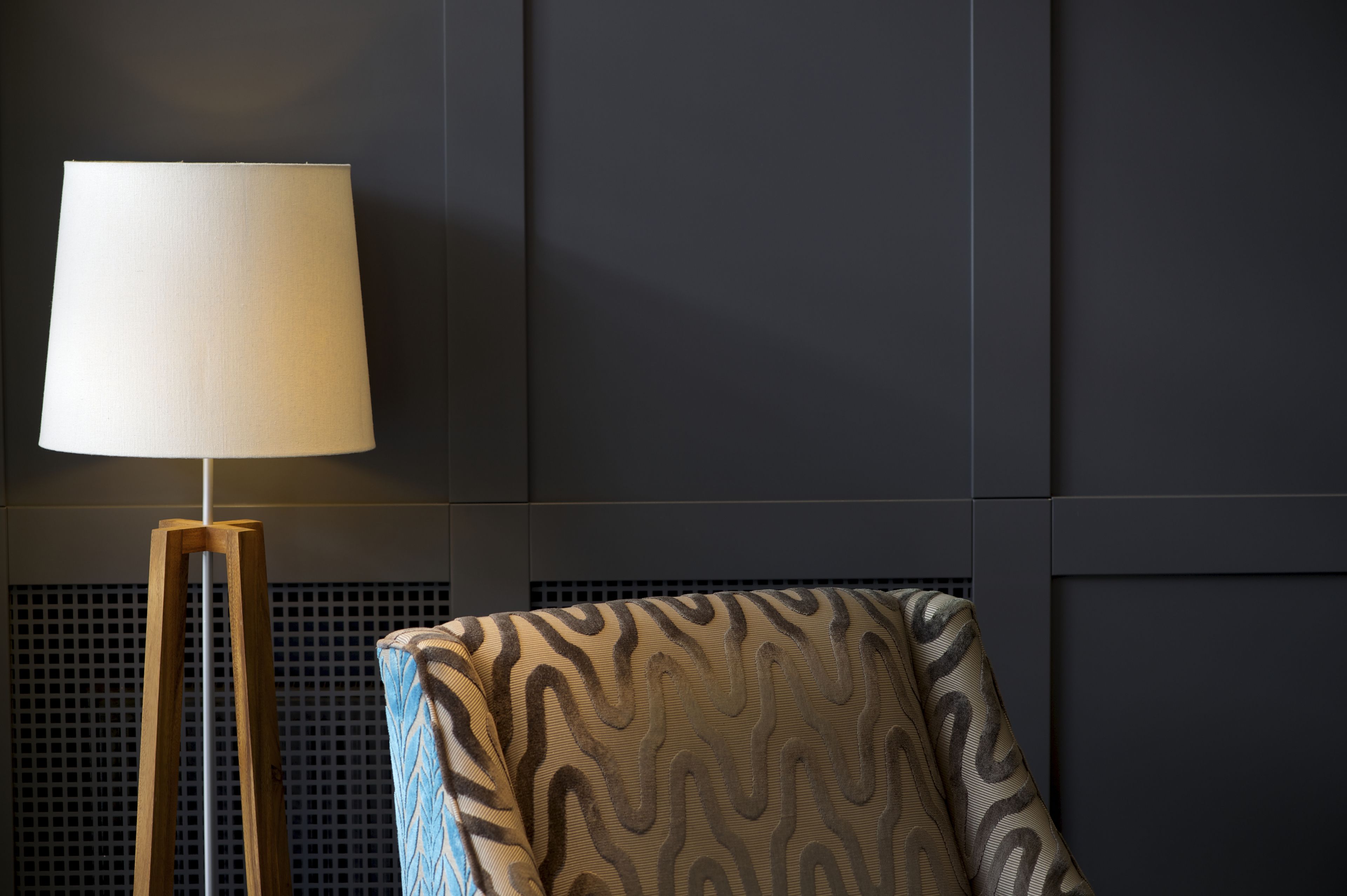 A modern room with a floor lamp, patterned armchair, and dark paneling on the walls.