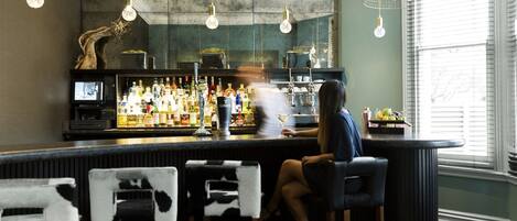 Uma área de bar com banquetas, balcão e uma tela de televisão.
