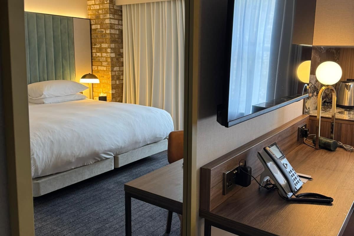 A hotel room with a bed, a desk with a telephone, a mirror, and a television.