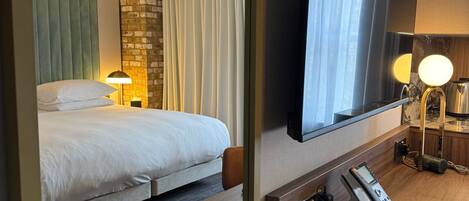 A hotel room with a bed, a desk with a telephone, a mirror, and a television.