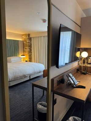 A hotel room with a bed, a desk with a telephone, a mirror, and a television. - The Lodge Hotel - Putney (London)