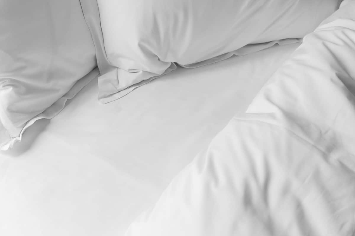 A close-up of a neatly made bed with white bedding, including pillows and a duvet.