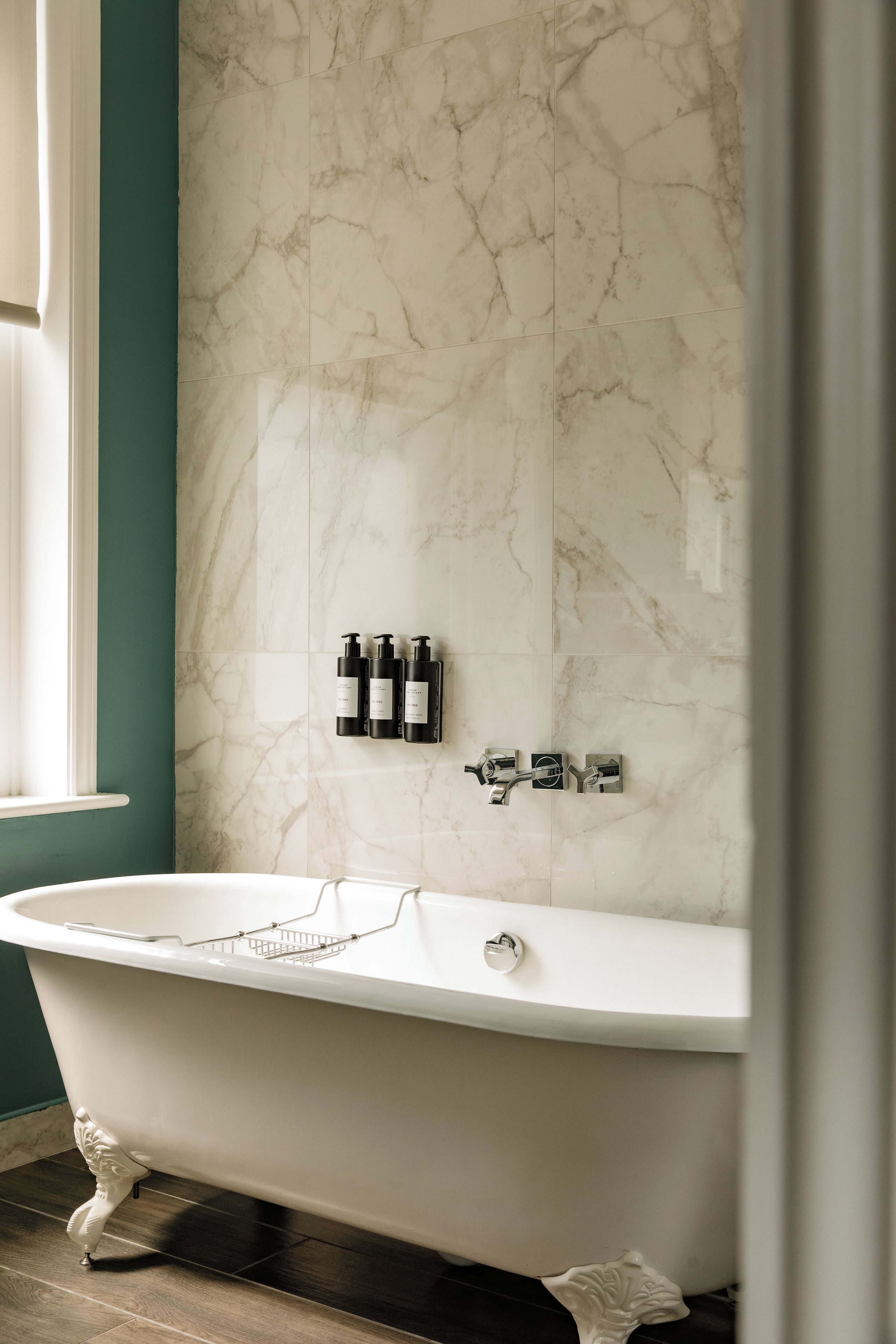 Ein Badezimmer mit einer freistehenden Badewanne, Marmorfliesen an den Wänden und einem Fenster.