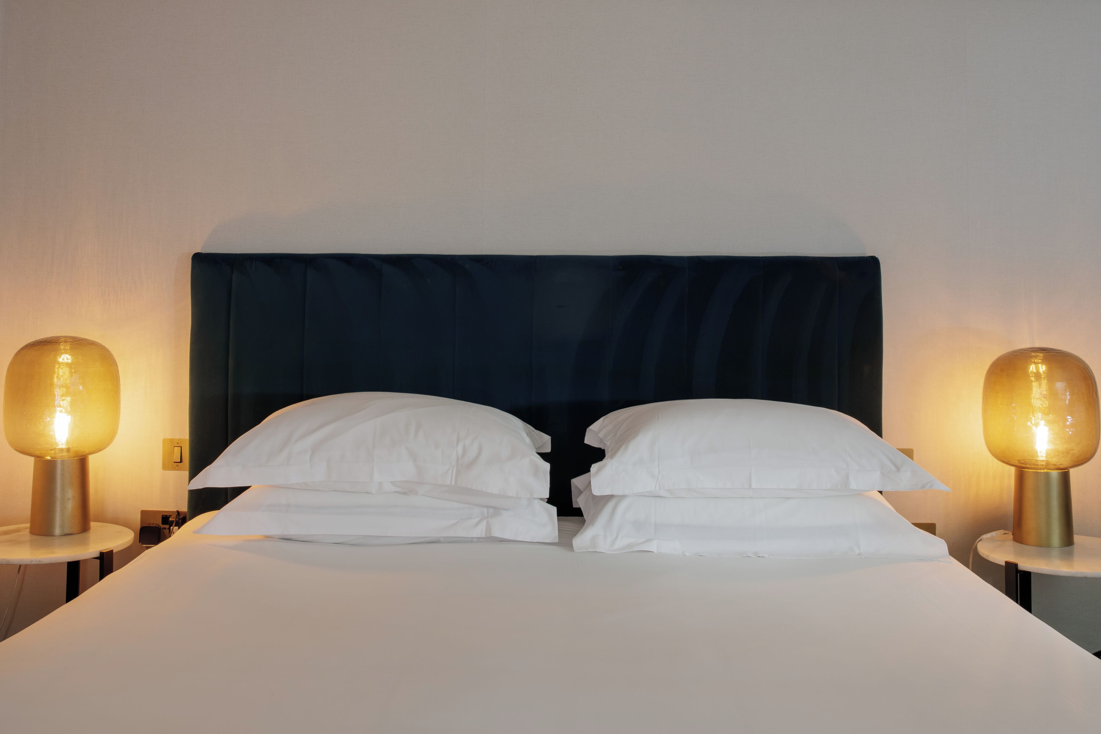 A double bed with white linens and two bedside lamps with round shades.
