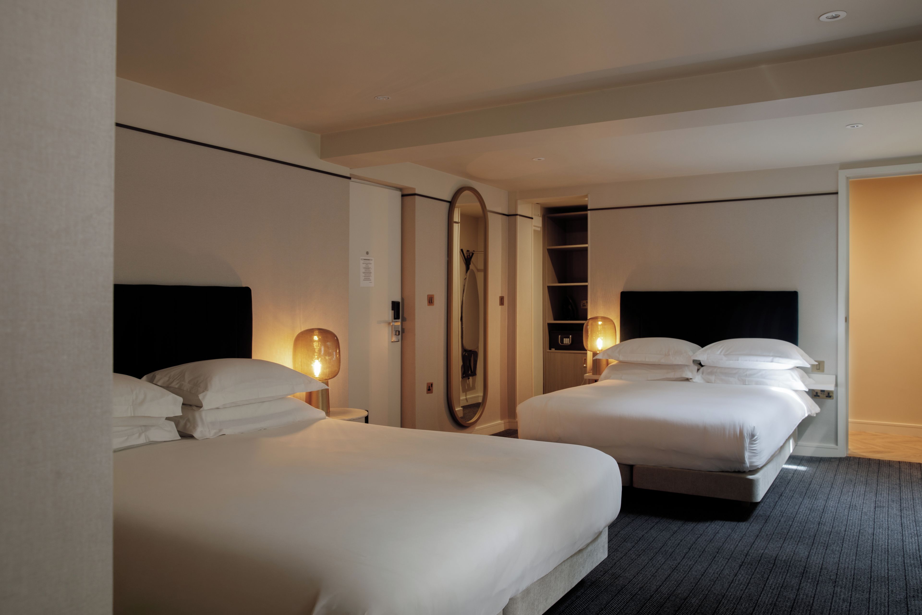 A hotel room with two beds, a wardrobe, a mirror, and a small seating area.