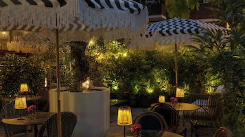 Un espace extérieur aménagé avec des tables et des chaises rondes, protégé par des parasols à motifs et entouré de verdure.
