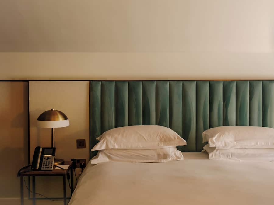 A hotel room with a bed, two pillows, a bedside table with a lamp, and a telephone.