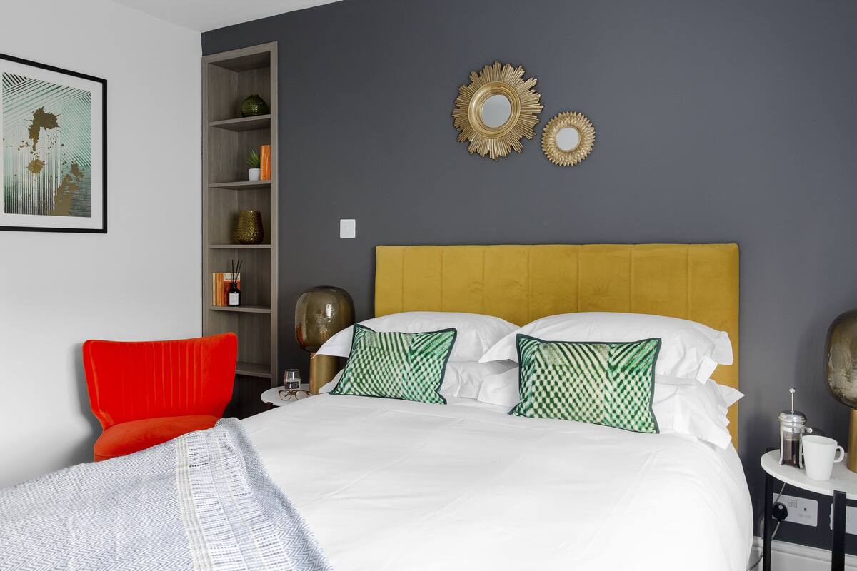A neatly arranged bedroom with a bed, a red chair, a bookshelf, and decorative mirrors on the wall.