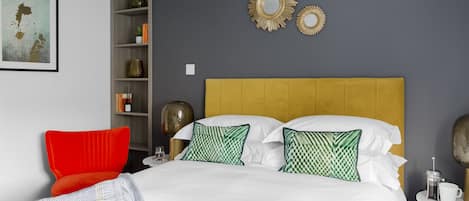 A neatly arranged bedroom with a bed, a red chair, a bookshelf, and decorative mirrors on the wall.