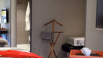 A hotel room with a bed, a wooden folding chair with a blanket, a suitcase, and a tray with a cup.