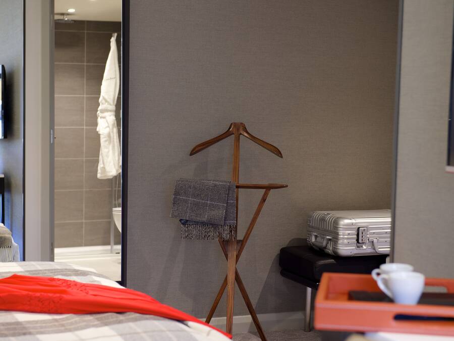 A hotel room with a bed, a wooden folding chair with a blanket, a suitcase, and a tray with a cup.