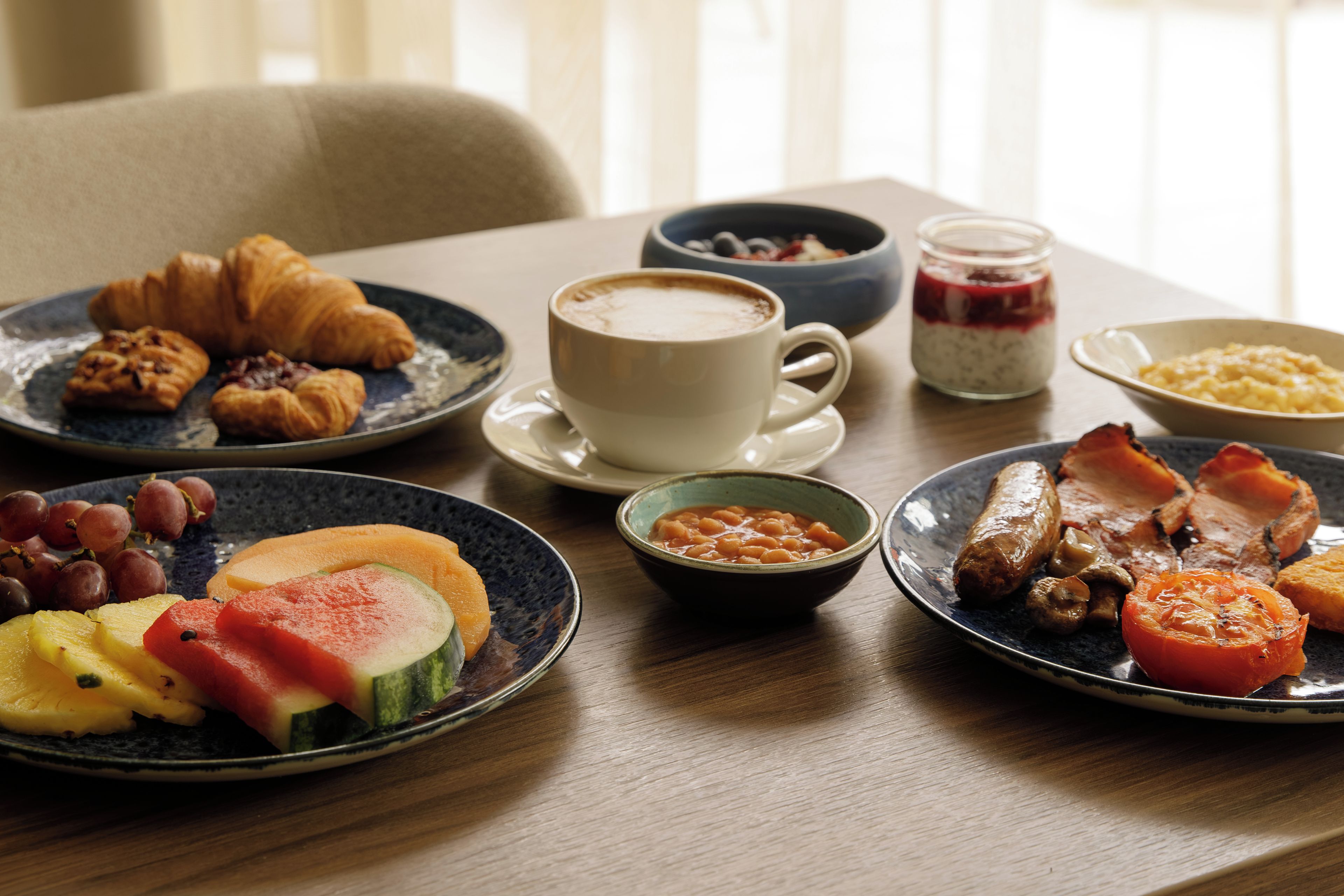 A breakfast table with croissants, coffee, fruit, and various dishes.