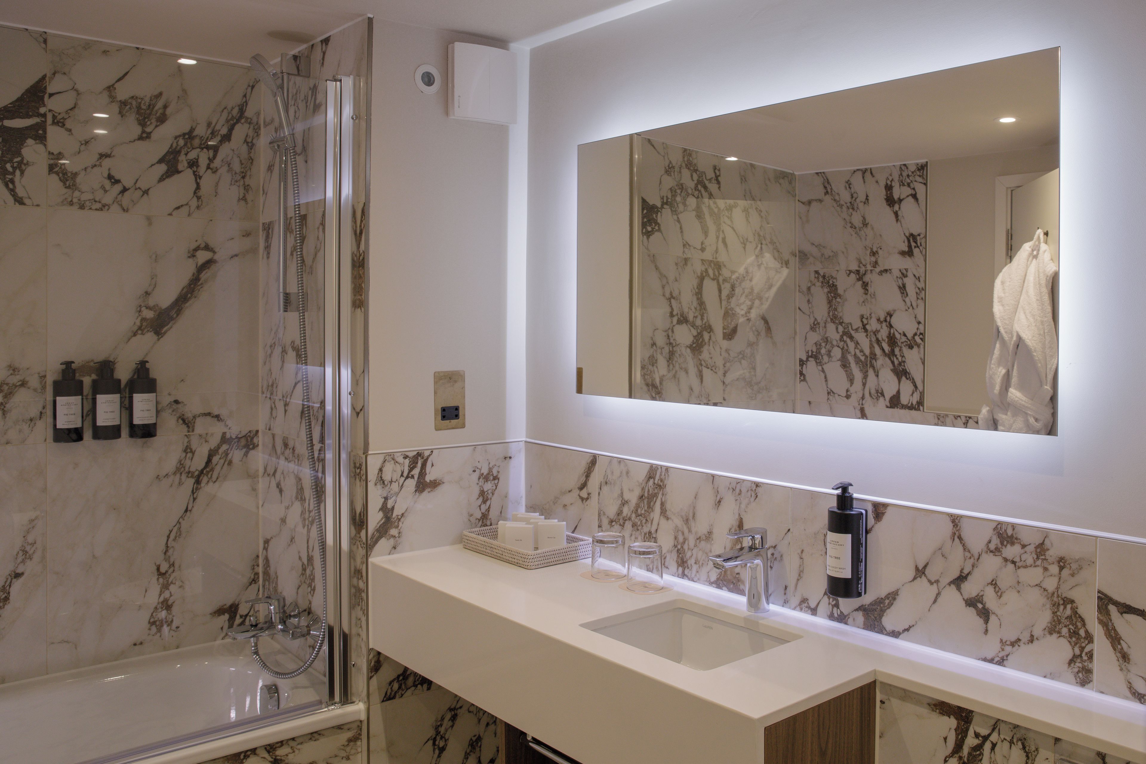 Un baño moderno con ducha envuelta en vidrio, un espejo grande y una pared revestida de mármol.