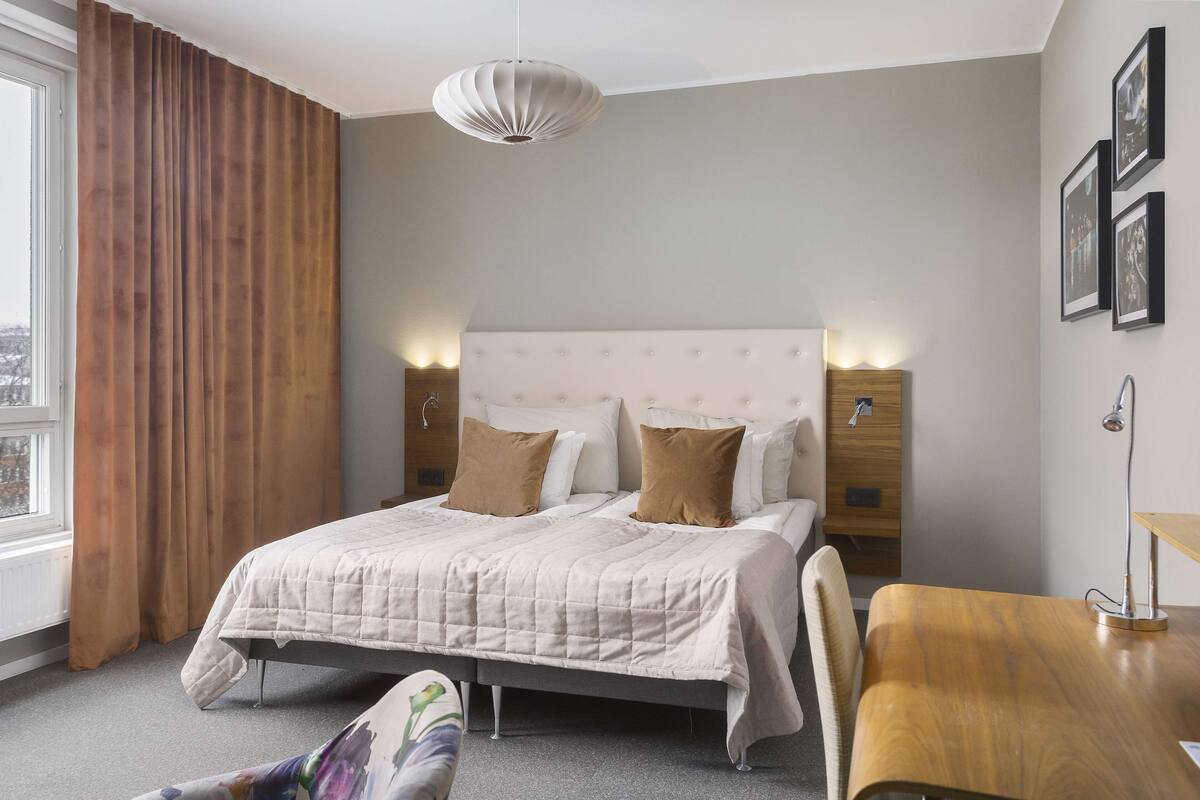Um quarto com cama, mesas de cabeceira, escrivaninha e uma cadeira.