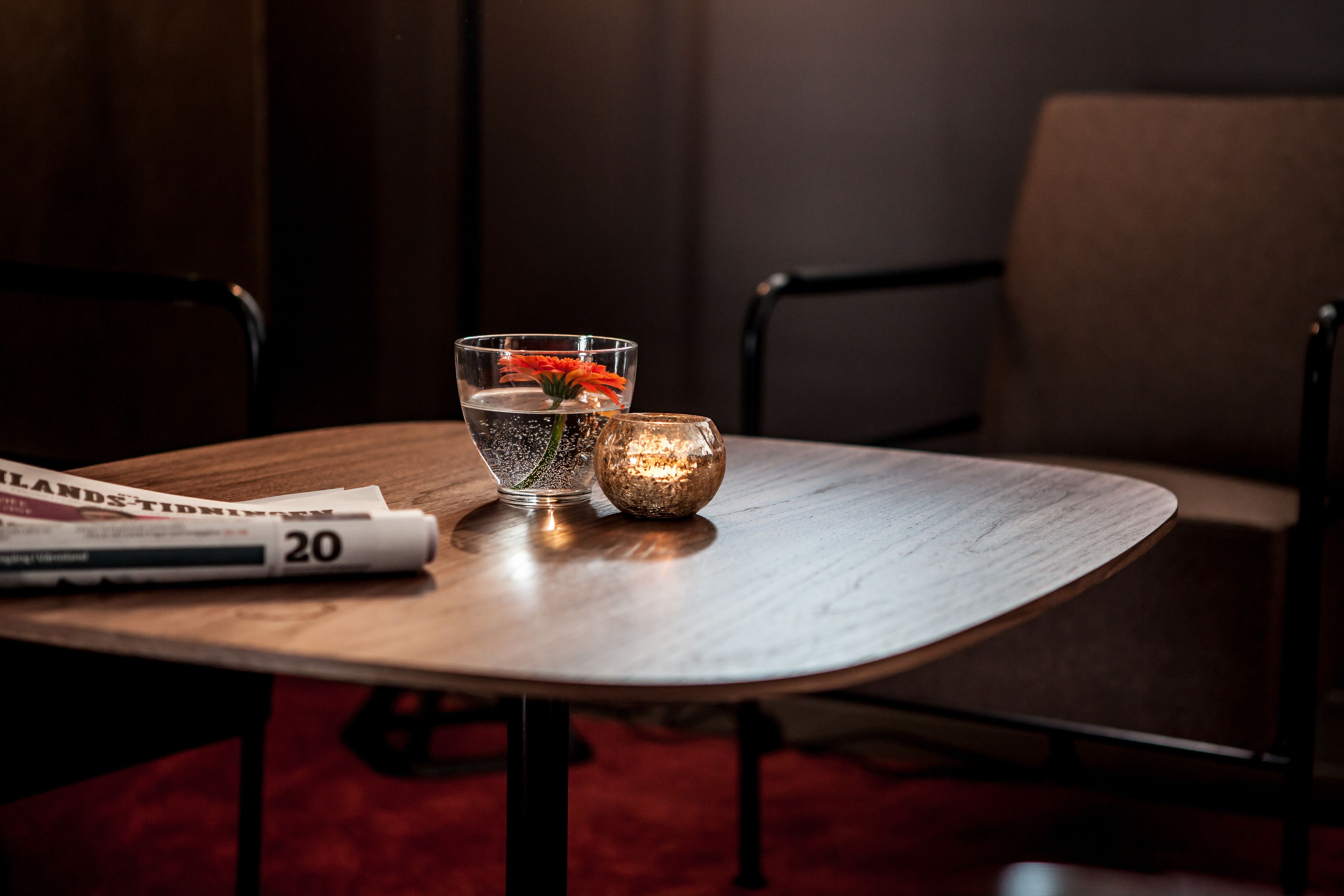 A round wooden table with a magazine, a glass with a flower, and a candle.