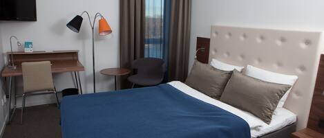 A hotel room with a large bed, a desk with a chair, a television, and a window with curtains.