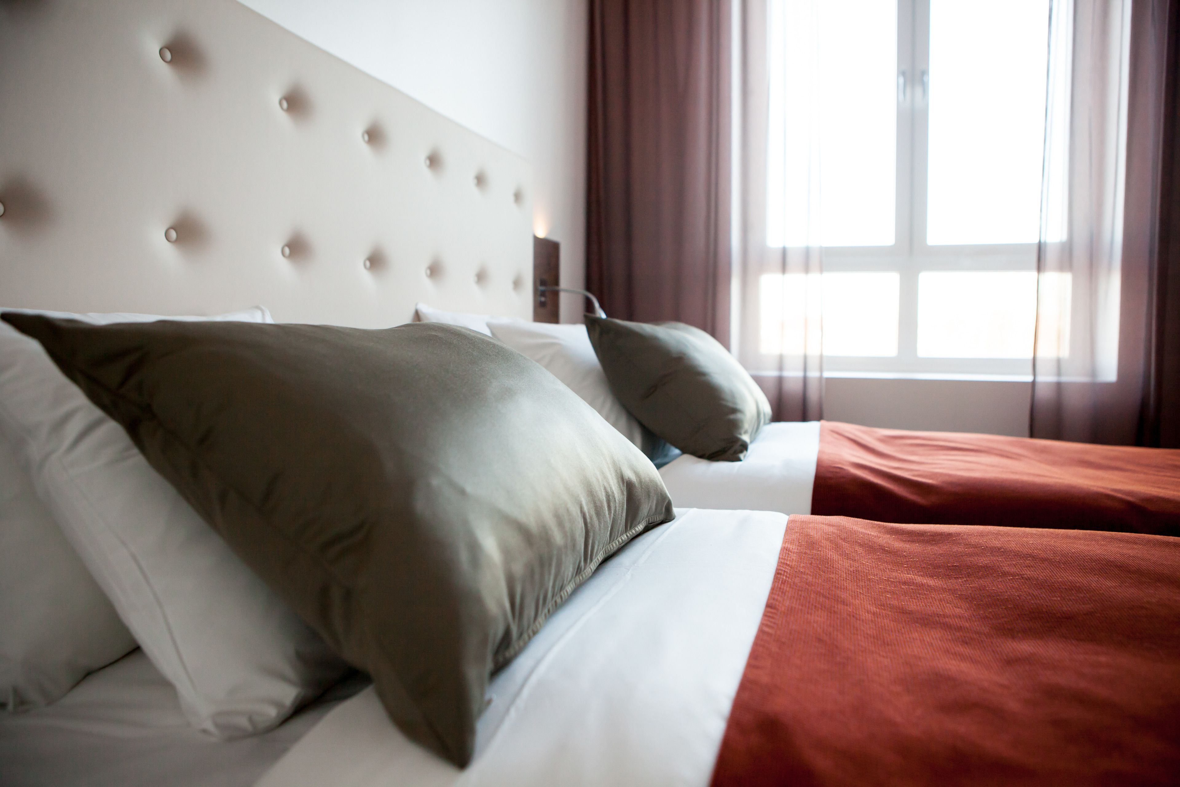 A hotel room with a bed, a headboard, and a window with curtains.