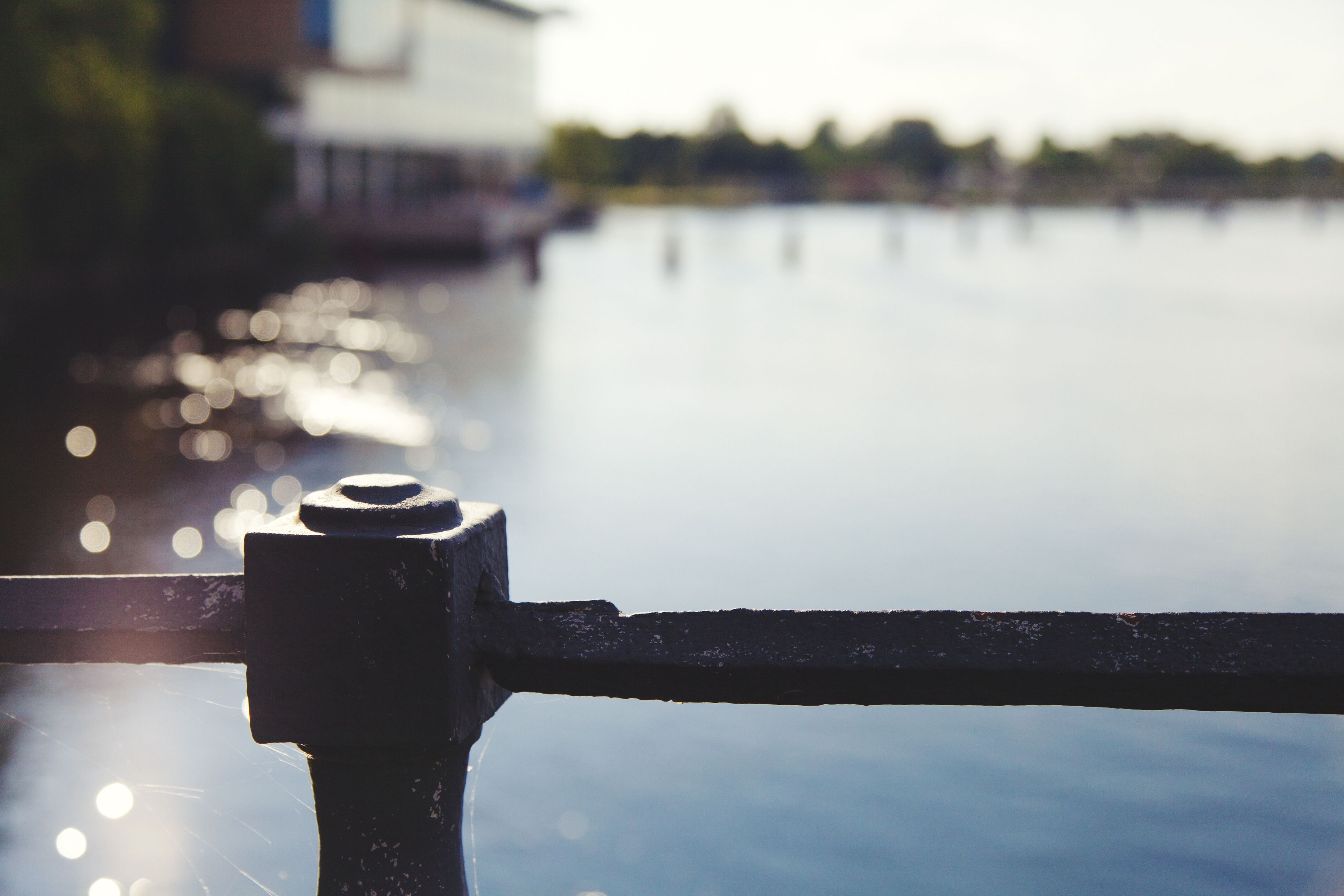 A metal railing by a calm body of water with a blurred background of buildings.