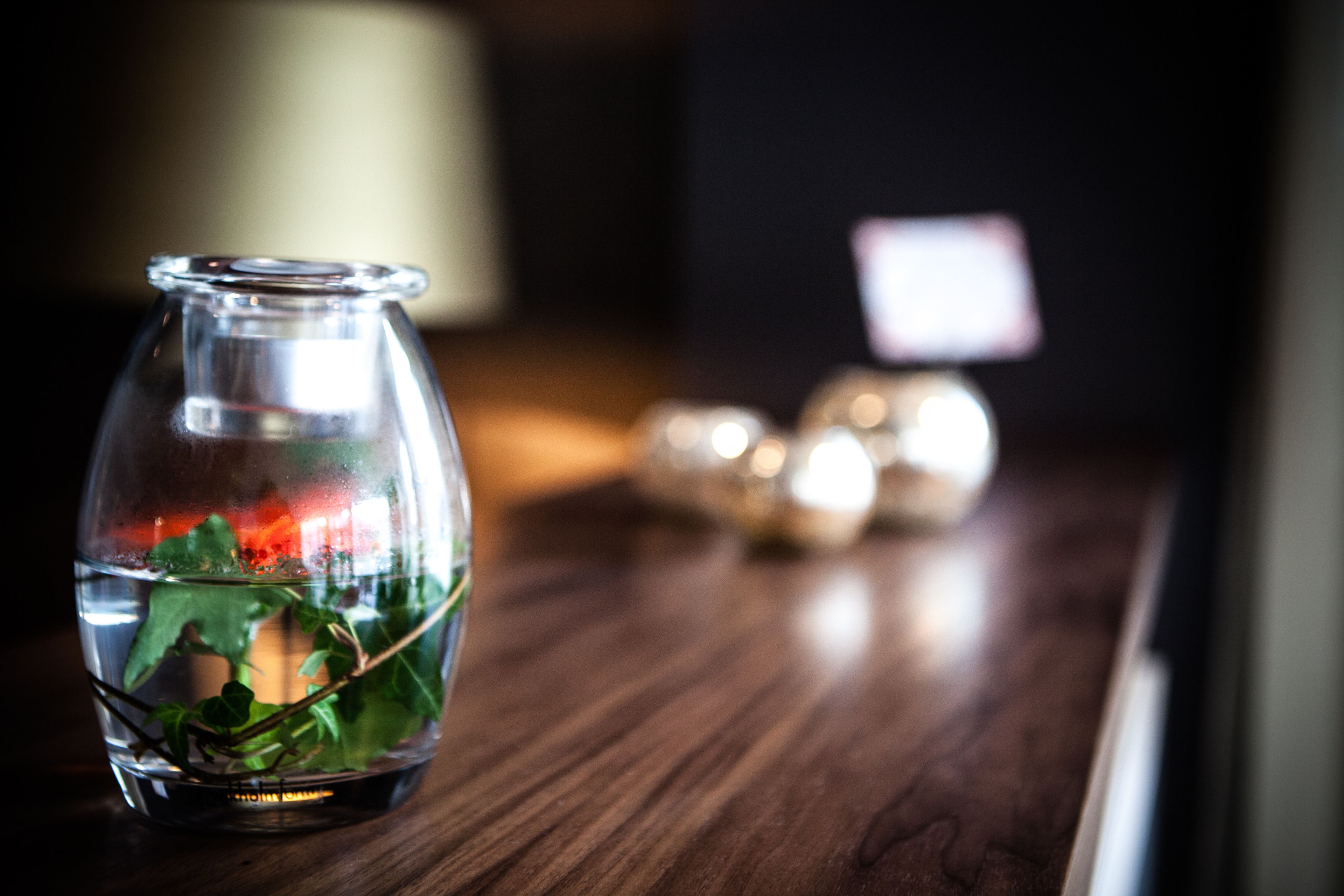 A clear glass bowl with water and green leaves on a wooden surface.