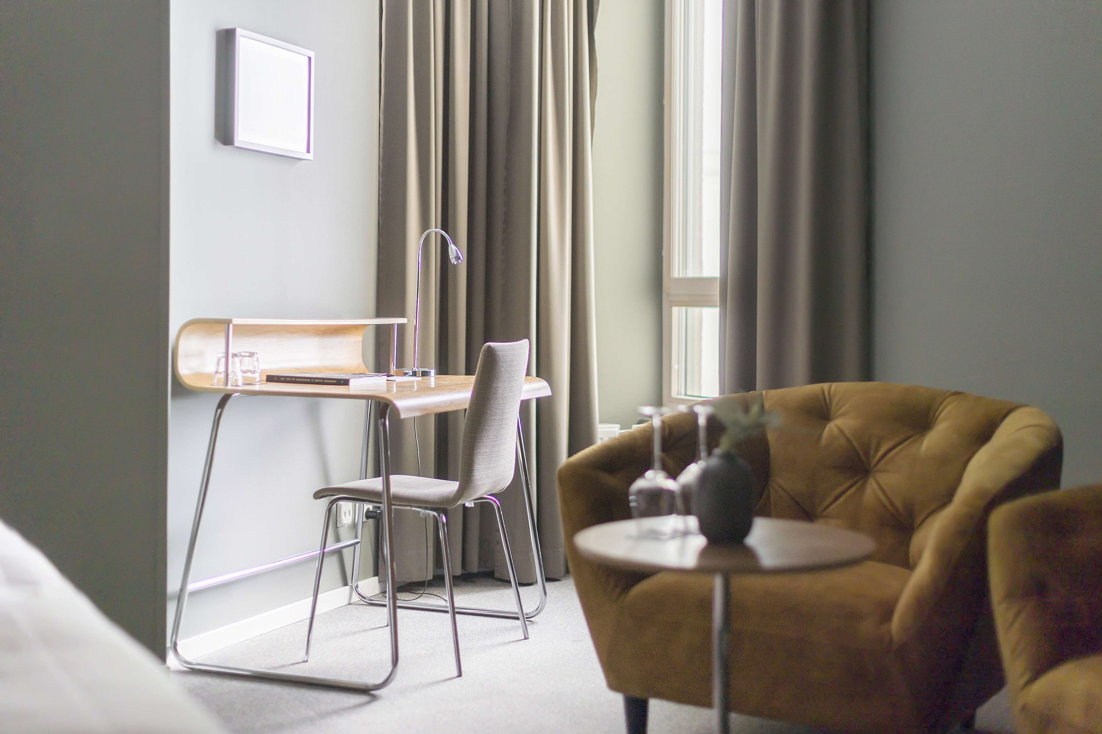 A modern hotel room with a desk, chair, and a round table with a vase.