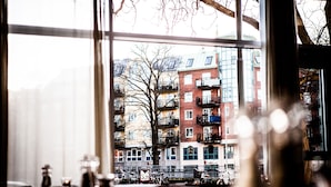 Vista a través de una ventana que muestra un edificio al fondo, un árbol y una calle con bicicletas.