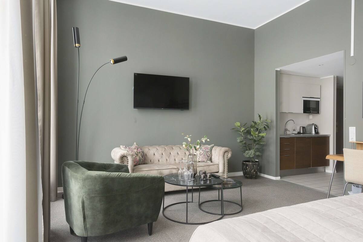 Uma sala de estar moderna com um sofá, uma poltrona verde, uma mesa de centro e uma televisão de tela plana fixada na parede.