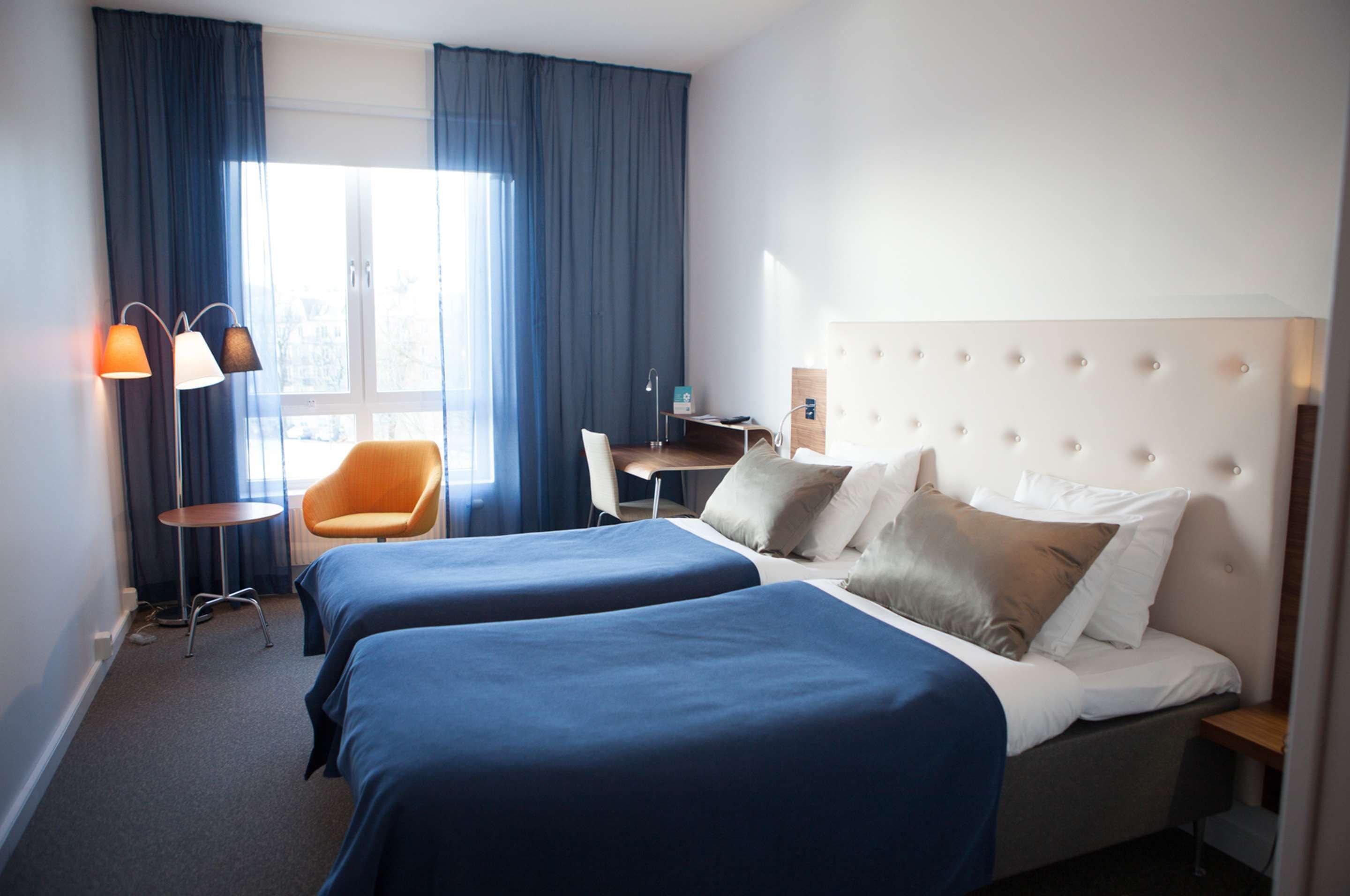 Una habitación de hotel con dos camas, un escritorio, una silla y una lámpara.