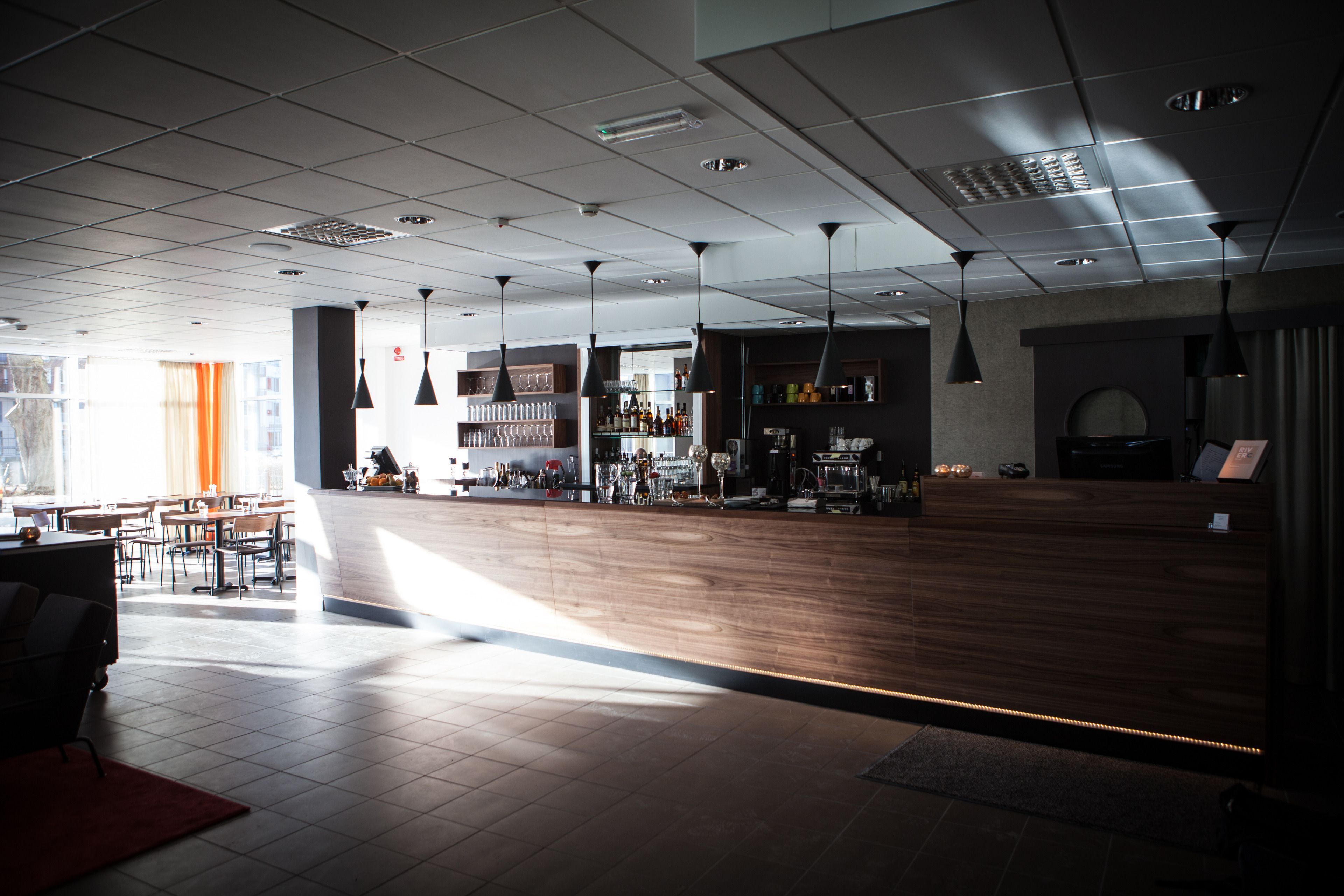 A spacious indoor area with a wooden reception desk, multiple seating areas, and a bar with shelves of bottles.