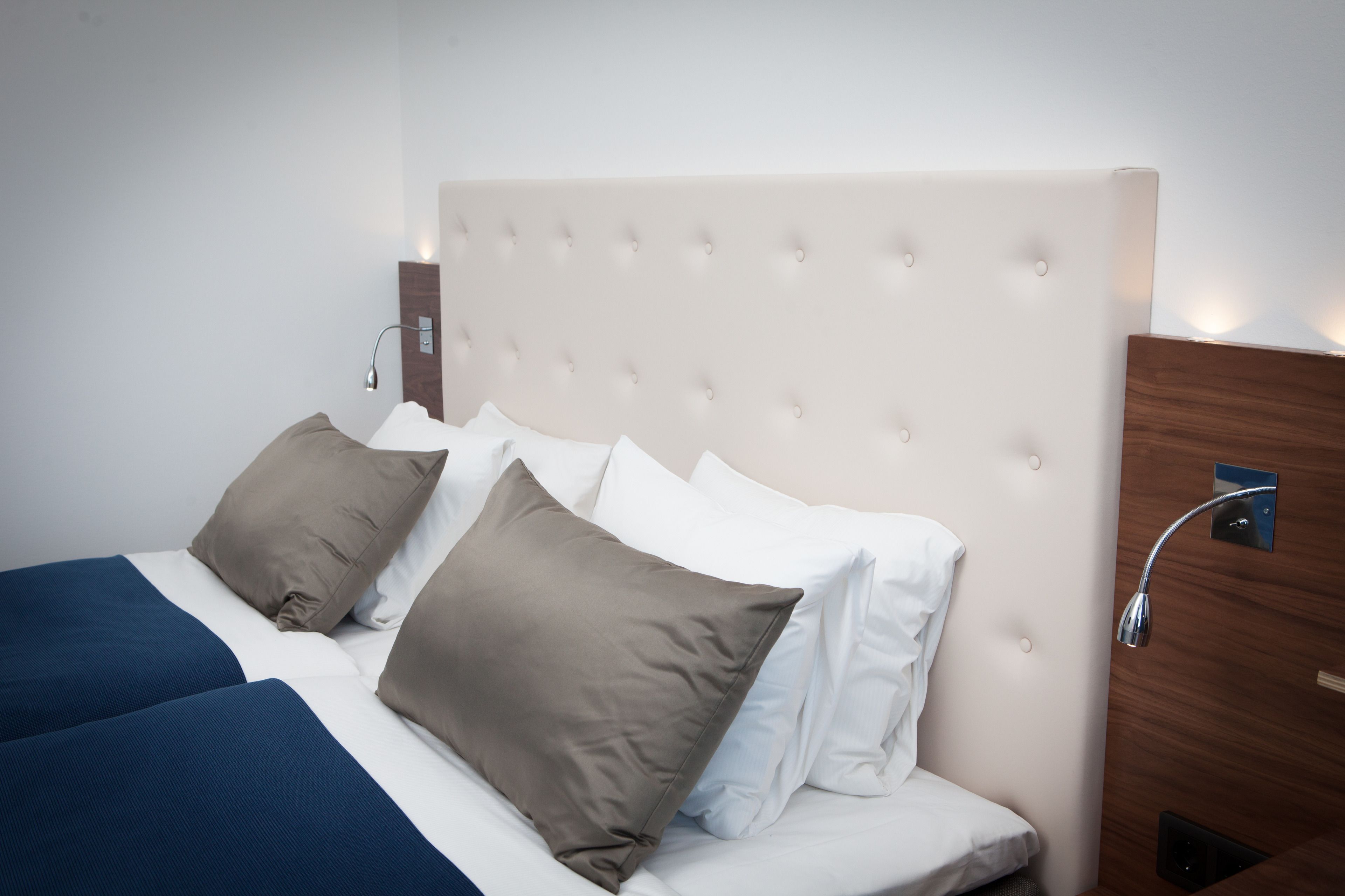 Una cama con cabecera capitonada, dos almohadas y una mesita de noche con una lámpara.