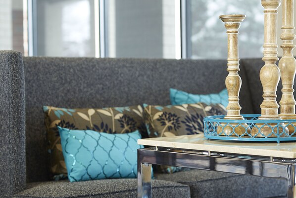 Una sala de estar moderna con un sofá gris, cojines estampados azules y una mesa de centro de vidrio transparente con una bandeja decorativa azul.
