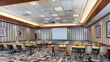 A conference room with multiple tables and chairs, a projector screen, and a patterned carpet.