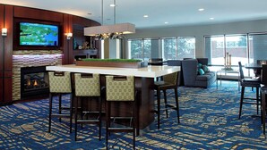 A modern bar area with a large TV, a fireplace, and a patterned carpet. - Courtyard by Marriott Woburn/Boston North (Woburn)