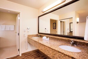 A hotel bathroom with a granite countertop, two sinks, a large mirror, and a shower area. - Courtyard by Marriott Woburn/Boston North (Woburn)