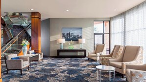 A hotel lobby with a patterned carpet, seating area with armchairs and sofas, a staircase, and a cityscape painting on the wall. - Courtyard by Marriott Woburn/Boston North (Woburn)