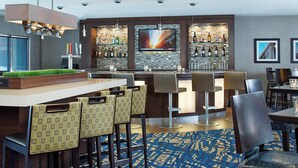 A modern bar area with a flat-screen TV, bar stools, and a variety of bottles on shelves. - Courtyard by Marriott Woburn/Boston North (Woburn)