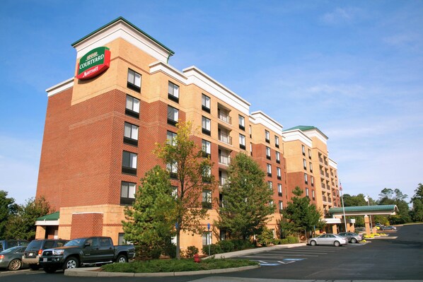 A Courtyard Marriott hotel with a brick facade, multiple floors, and a parking lot with several cars. - Courtyard by Marriott Woburn/Boston North (Woburn)