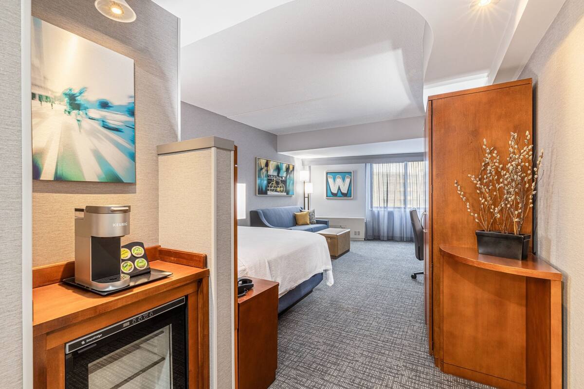 A hotel room with a kitchenette, a bed, a seating area, and a large window.