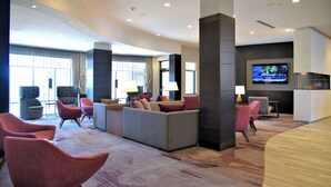 A modern hotel lobby with a seating area, a flat-screen TV, and a reception desk. - Courtyard by Marriott Boston Waltham (Waltham)