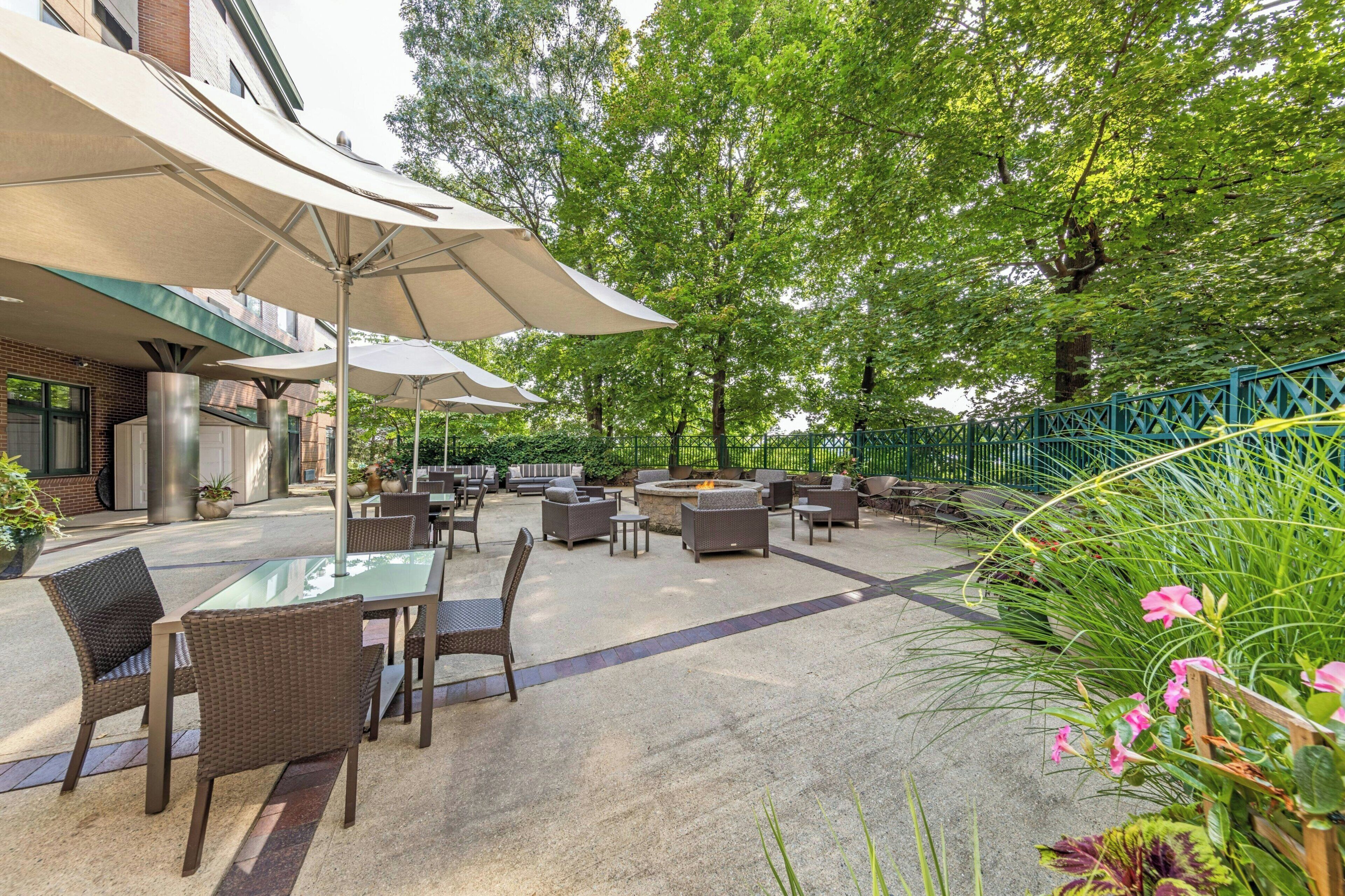 An outdoor patio area with tables and chairs, umbrellas, and a fire pit.