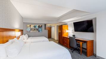 Habitación de hotel con dos camas, un escritorio, un televisor y un cuadro en la pared.